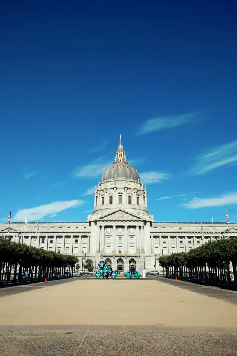 A civic government building with flags flying on the plaza in front of it